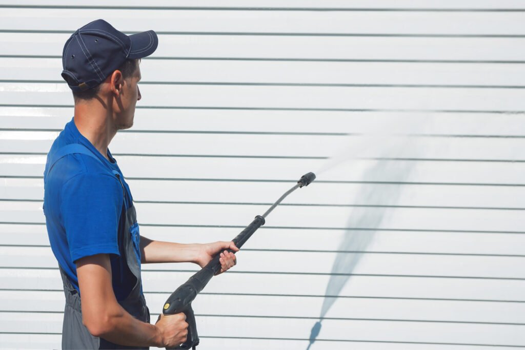 Worker in overalls washes a white wall from a siding with a water gun Power washing white siding in Wheeling IL area